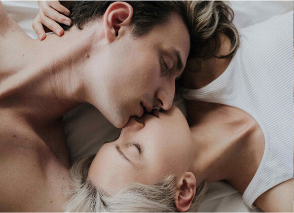 A man and a woman enjoying and relaxing on a bed after a sexual performance, closing their faces and lips with a kiss.