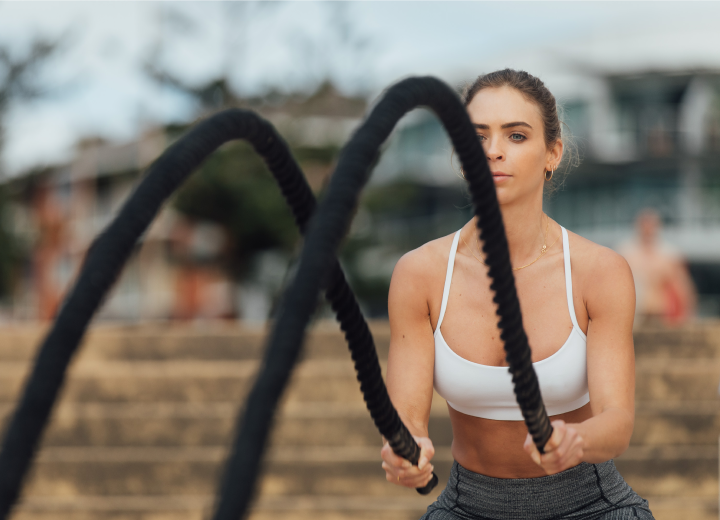 A woman firmly holds a rope, gearing up for a physical training session outdoors with a blurred background.