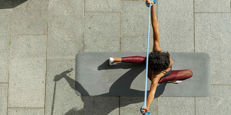 Down shot - Women performing yoga stretches on a mat in an outdoor setting during the daytime with sunshine.